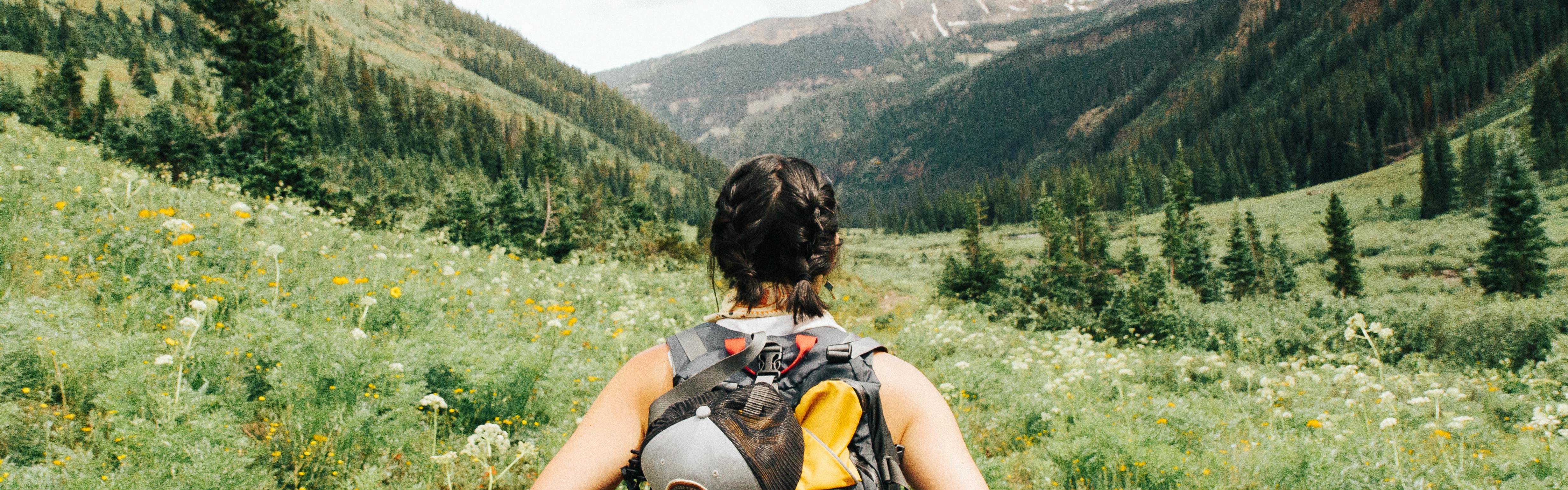 A woman in a tanktop hikes away from the camera while wearing a backpack.