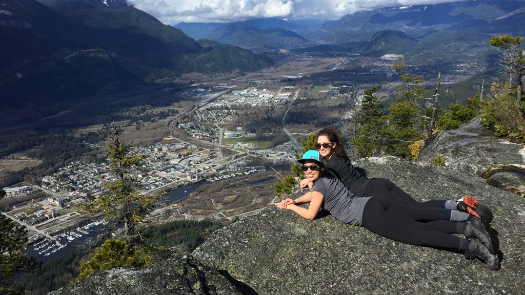 Two women smile at the camera in front of the view of Squamish, BC