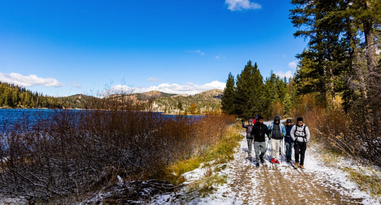 Several people walking on a snowy trail next to a lake. 
