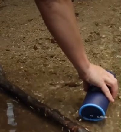 A hand filling up a water bottle in a stream.
