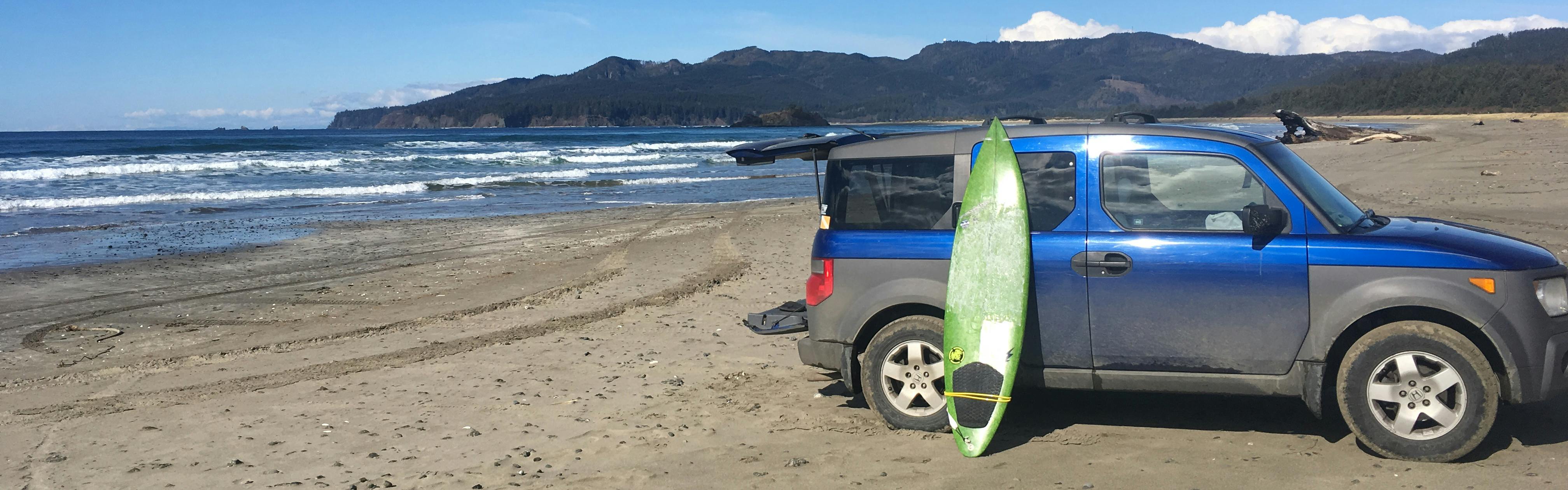 A blue SUV on the beach with a green surfboard