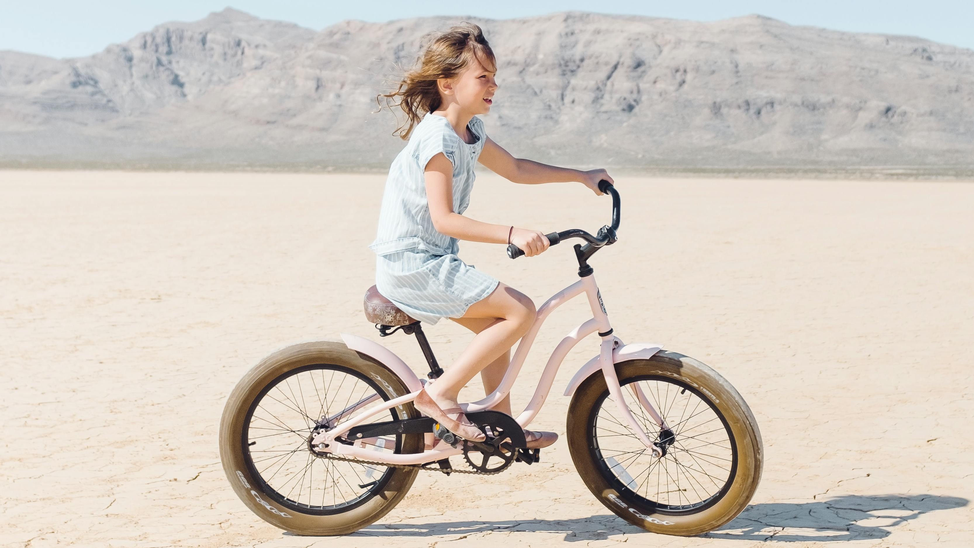 A girl rides a bike across a dried lake bed in a desert ecosystem. 