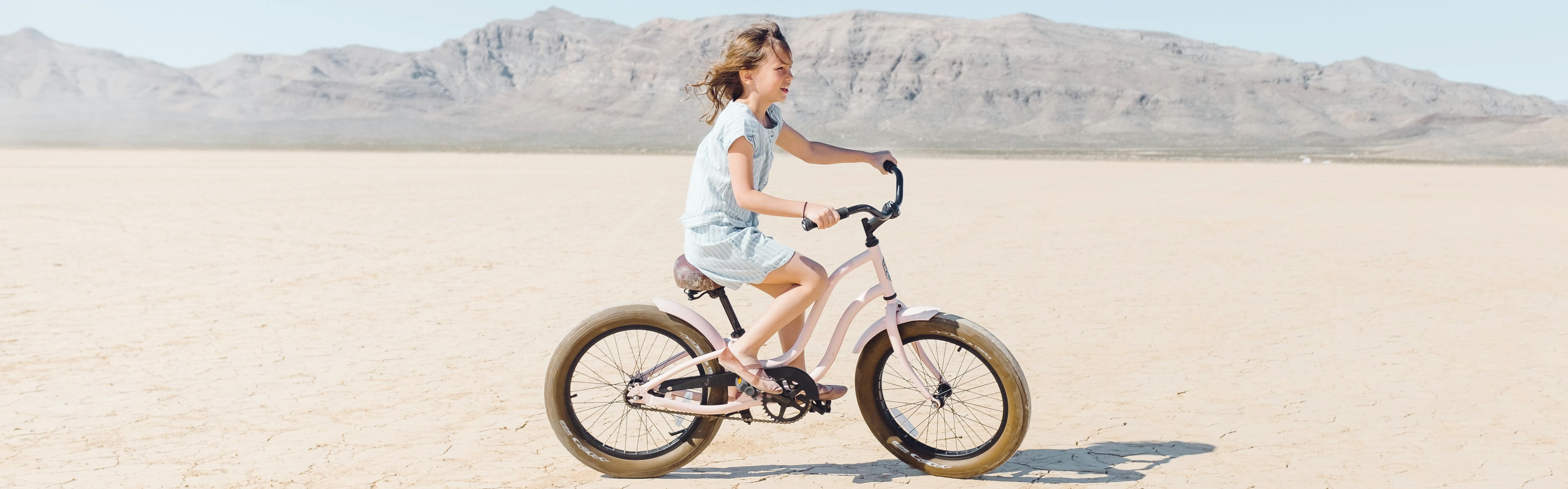 A girl rides a bike across a dried lake bed in a desert ecosystem. 