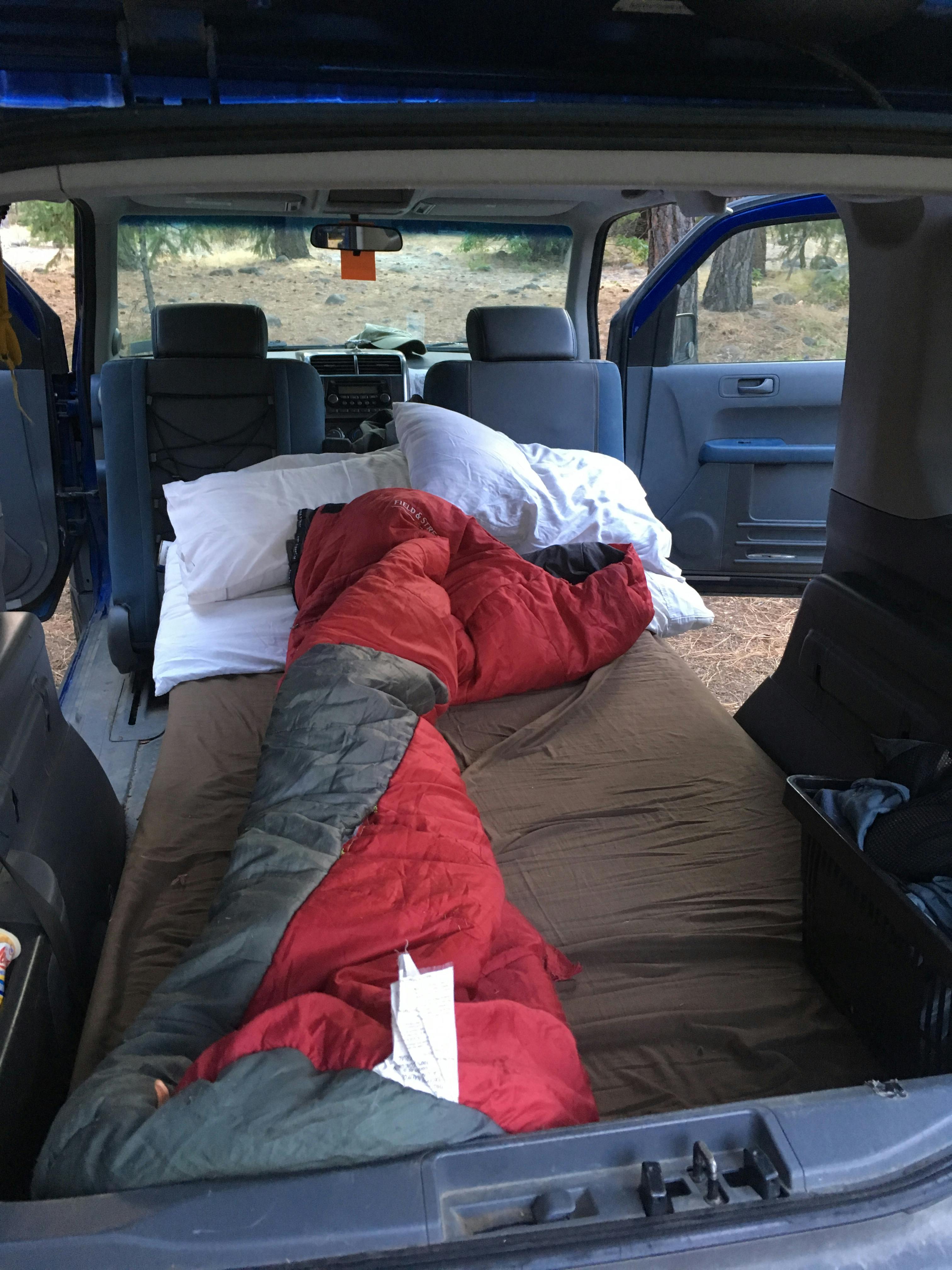 A red and grey sleeping bag on a sleeping pad set up inside an SUV