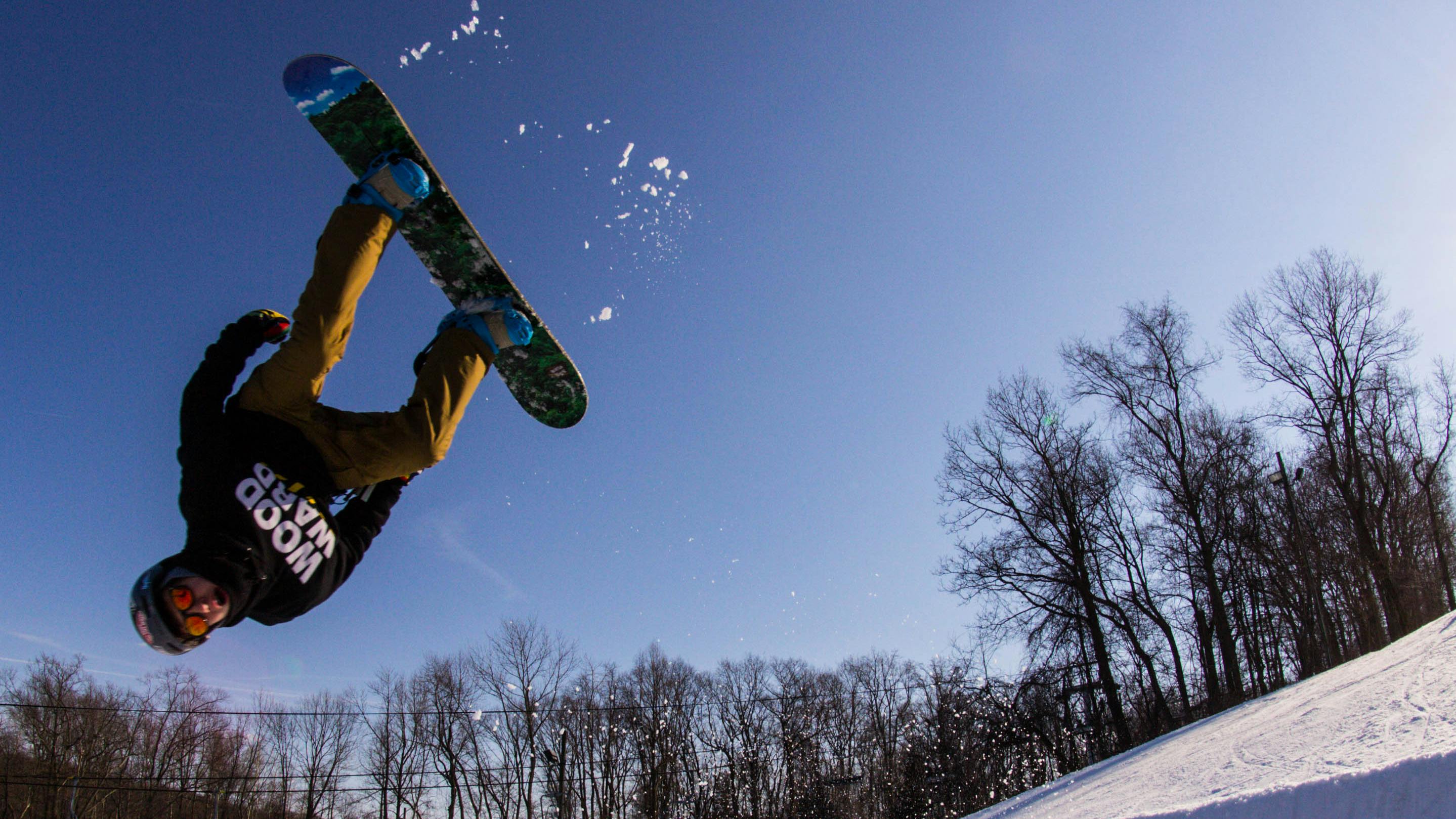 A snowboarder in a black sweatshirt executes a flip