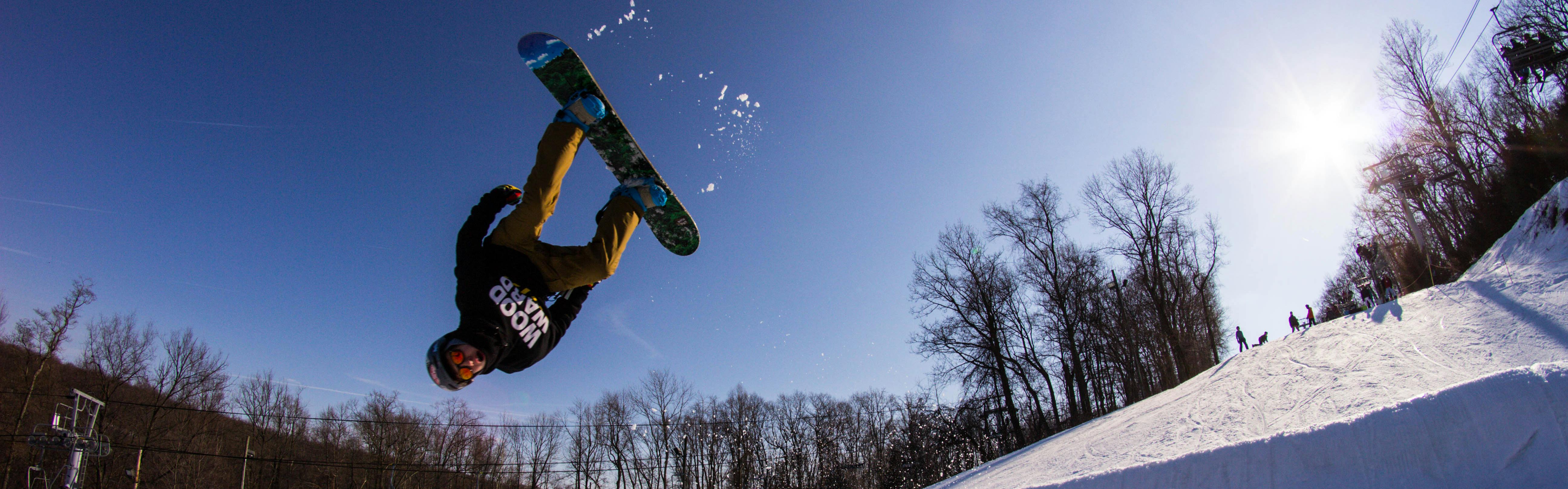 A snowboarder in a black sweatshirt executes a flip