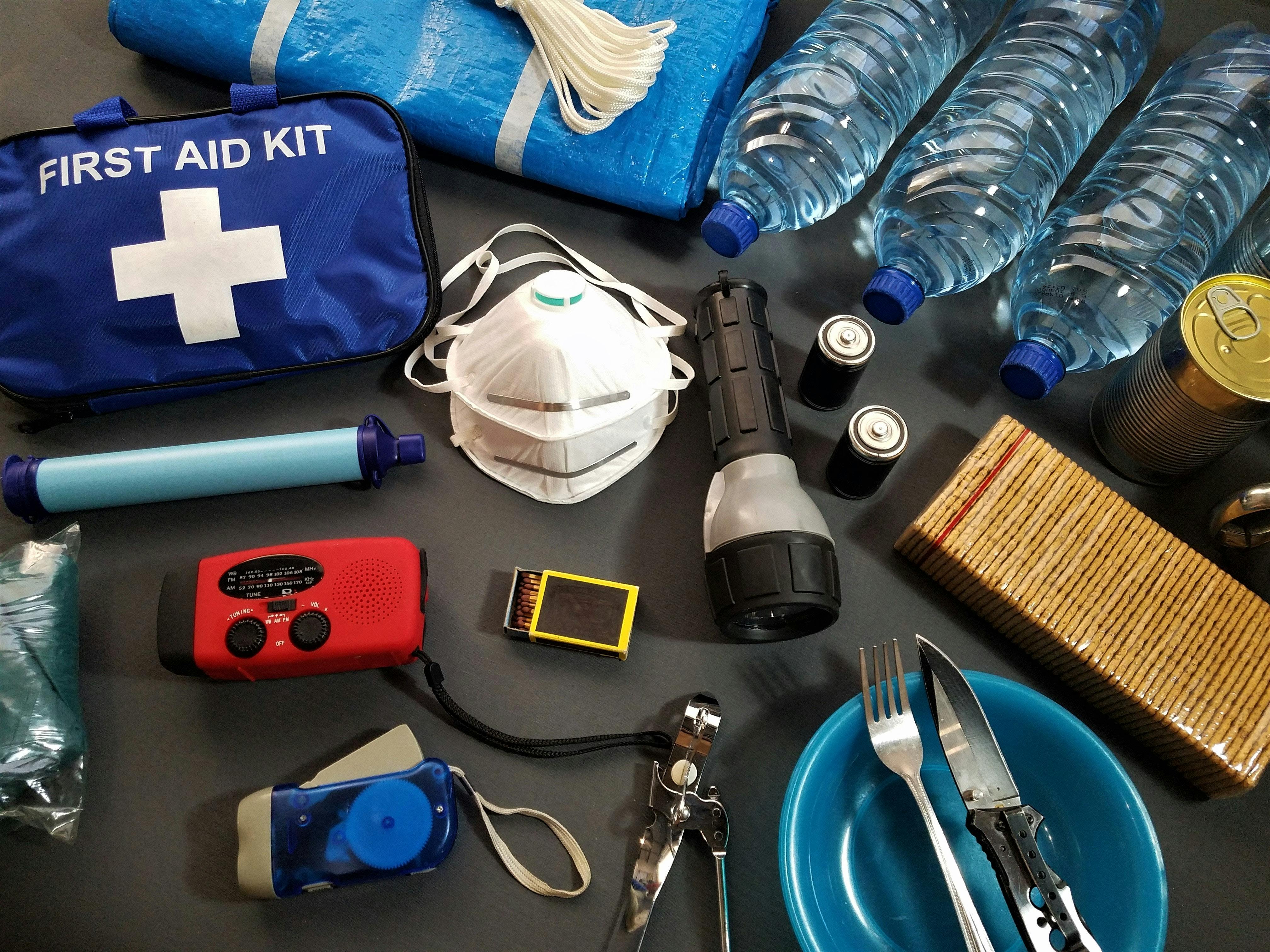 A blue first aid kit, three water bottles, a mask, crackers, utensils, a box of matches, a flashlight, two batteries, and other gear