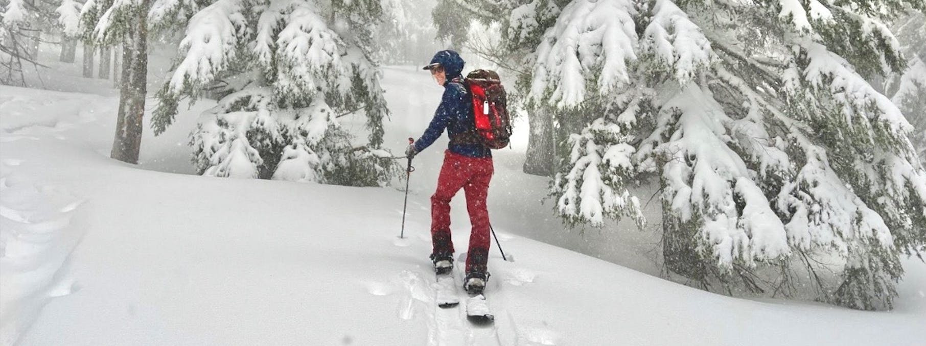 A woman splitboarding on a snowy day. She is walking uphill and smiling at the camera. 