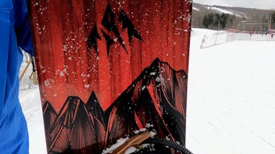 Closeup on the black mountains against red background graphics of the Jones Mountain Twin snowboard