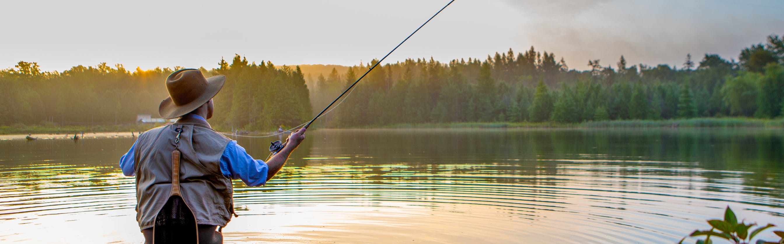 A fly fisherman standing in a lake at sunset