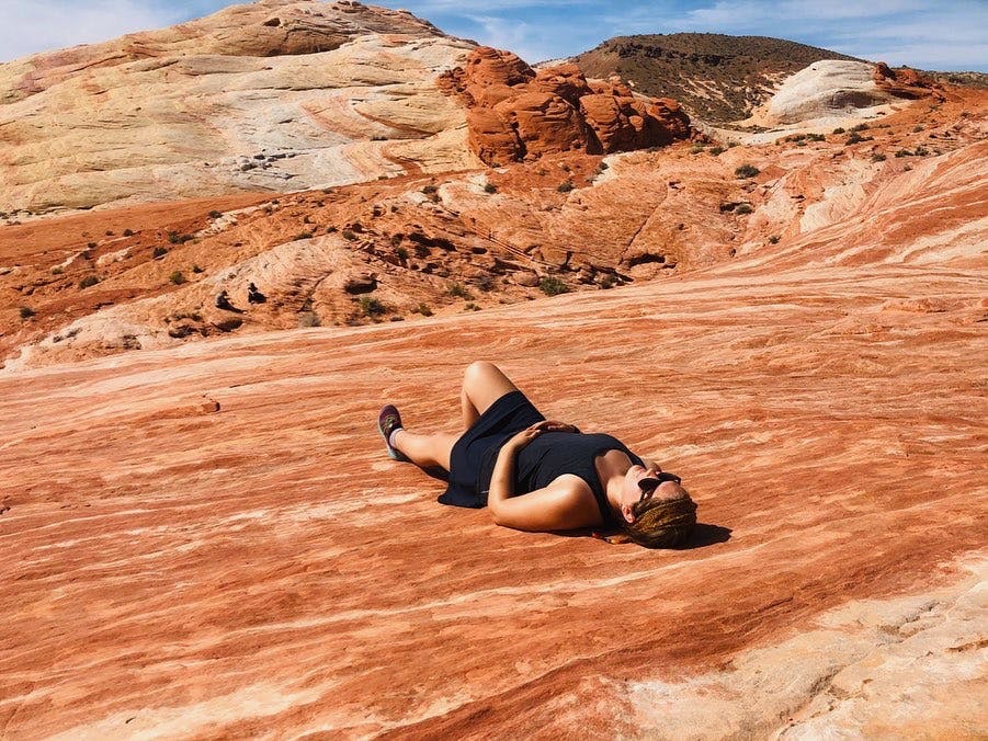The author lays on a red rock wave and basks in the sun while wearing a black hiking skirt.