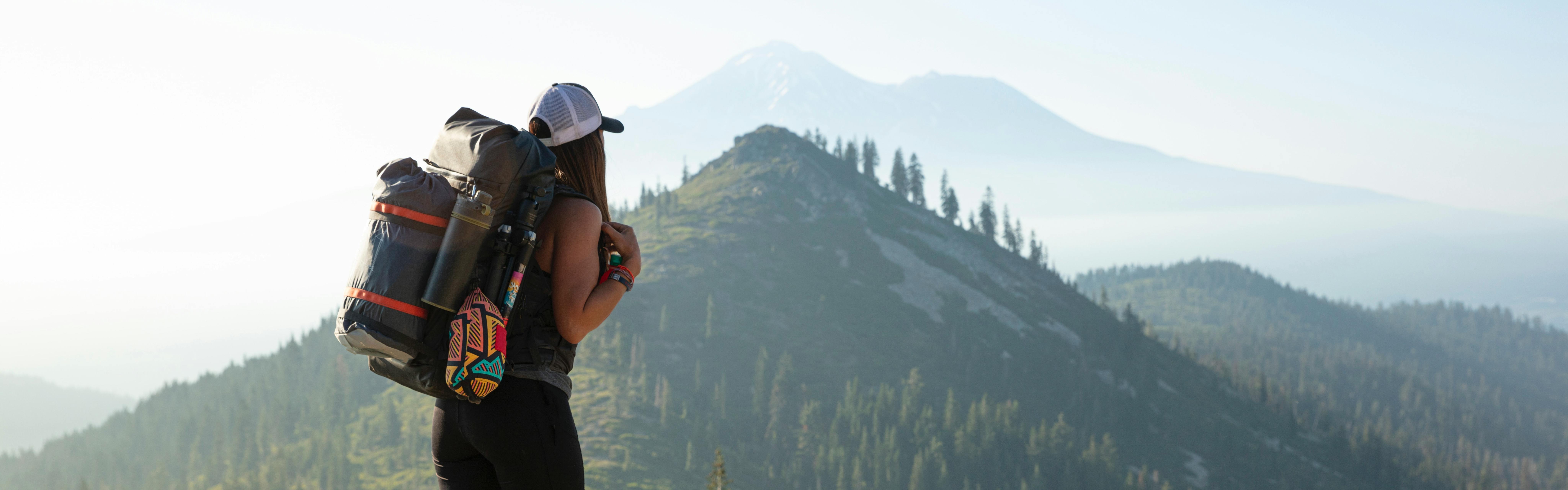 A woman stands with a backpacking pack on and looks toward mountains in the background.