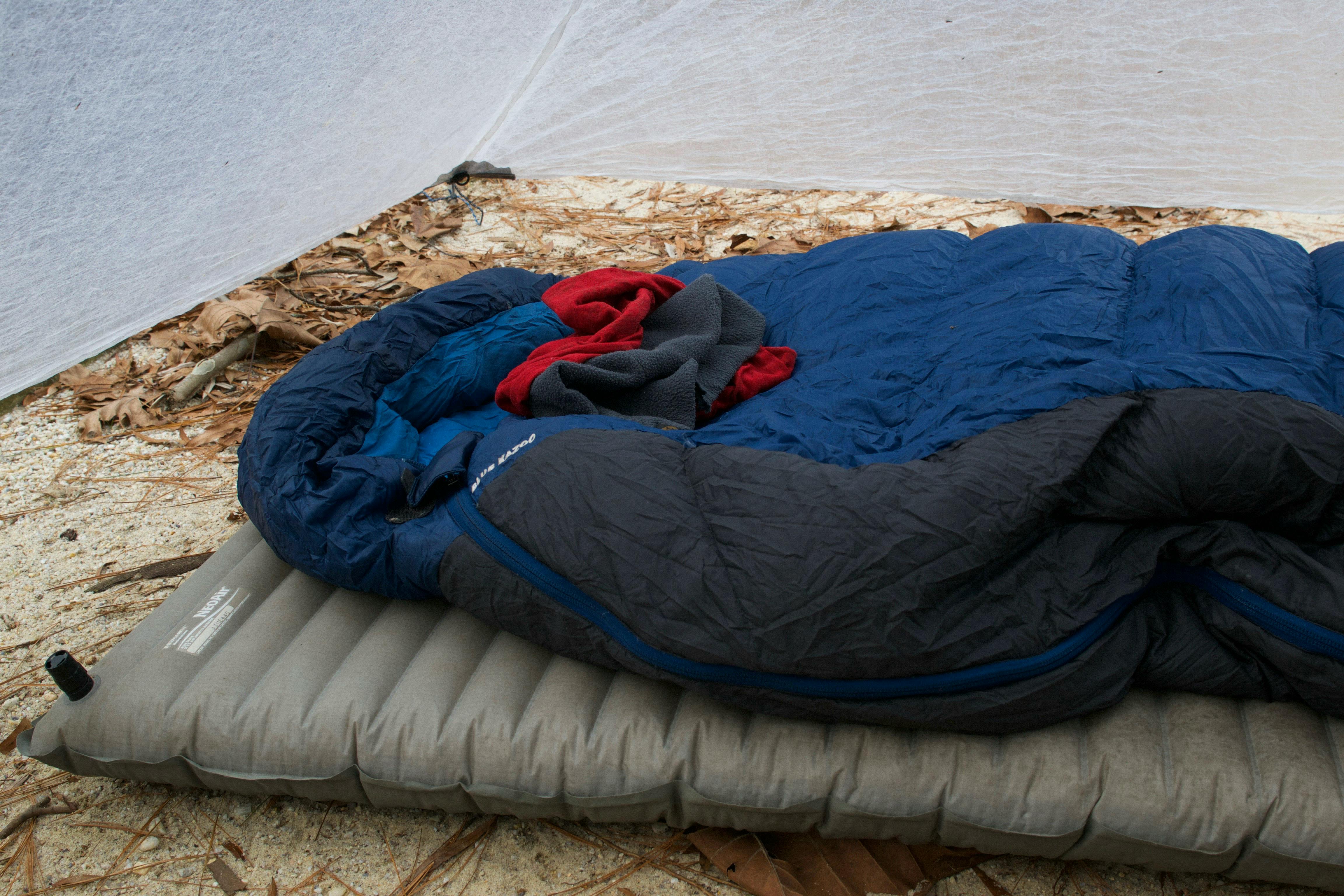 A sleeping bag and a sleeping pad lie on the ground. The sleeping bag is blue.