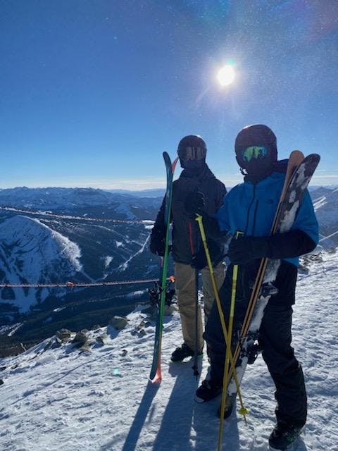 Two skiers stand with their skis at the top of a mountain.