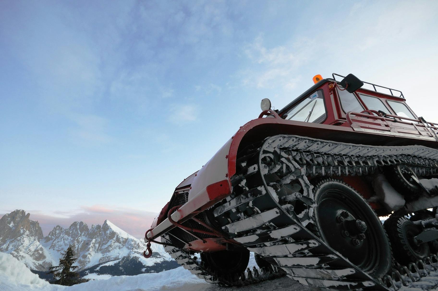 A red snowcat stands tall. In the background, we can see jagged mountain peaks. 