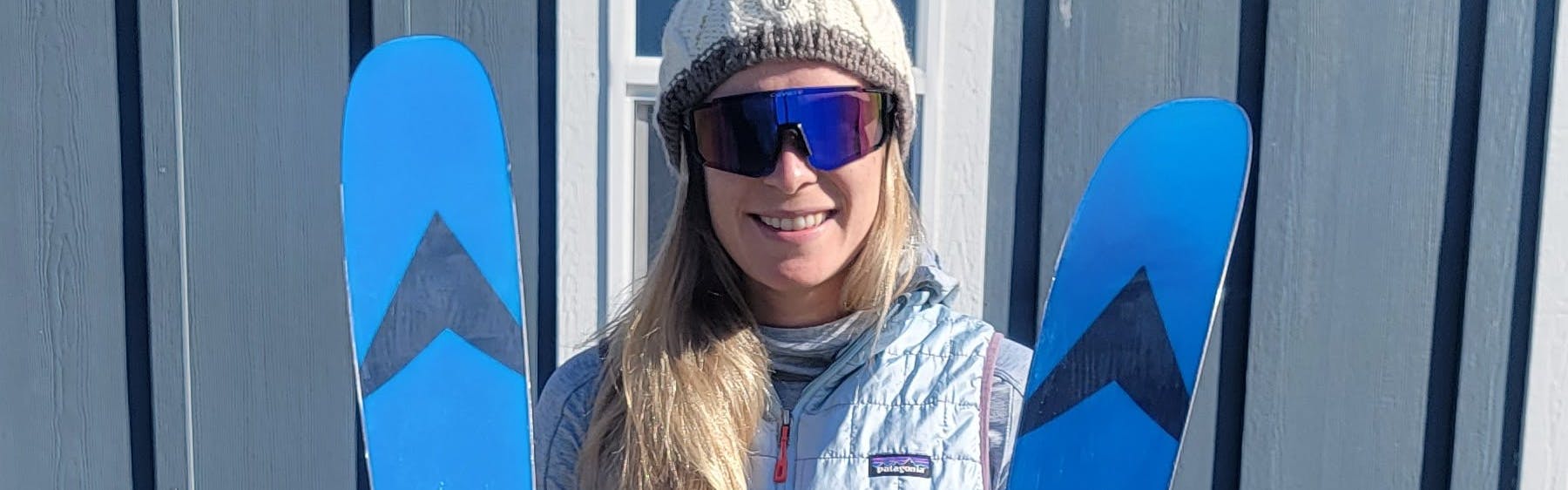 A woman standing smiling while holding the  Dynastar M-Free 99 Skis.