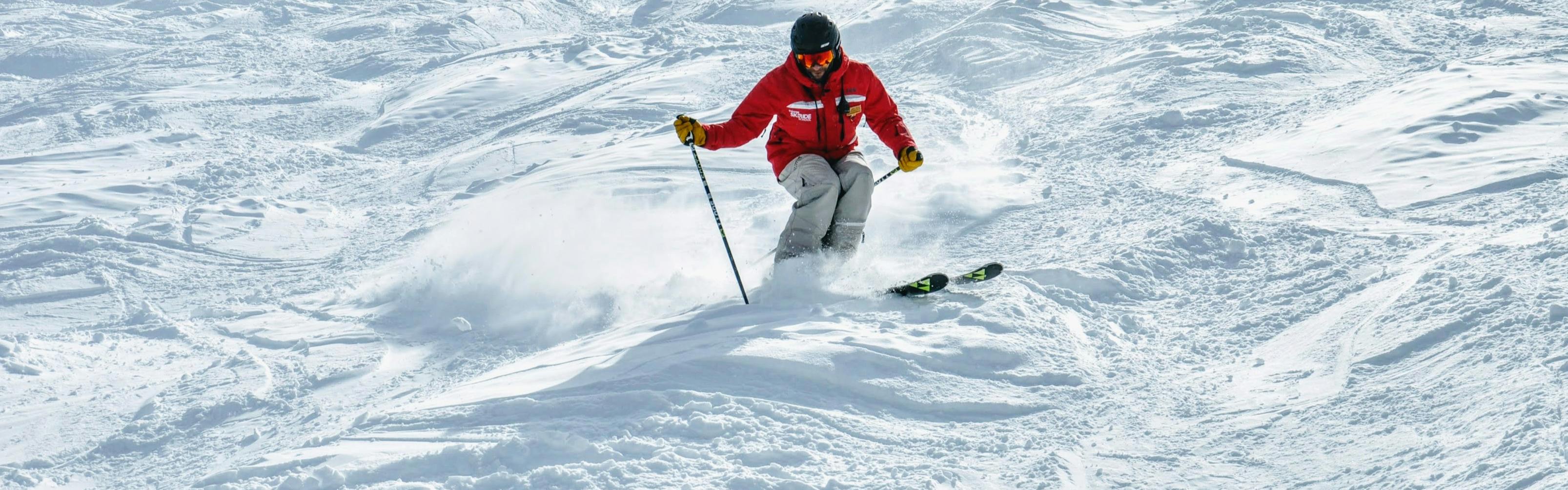 A skier in a bright red jacket skiing down moguls.
