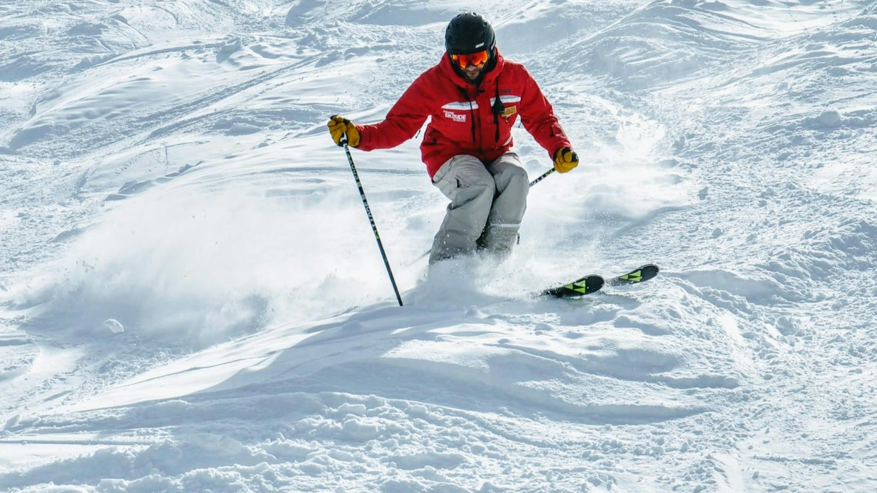 A skier in a bright red jacket skiing down moguls.
