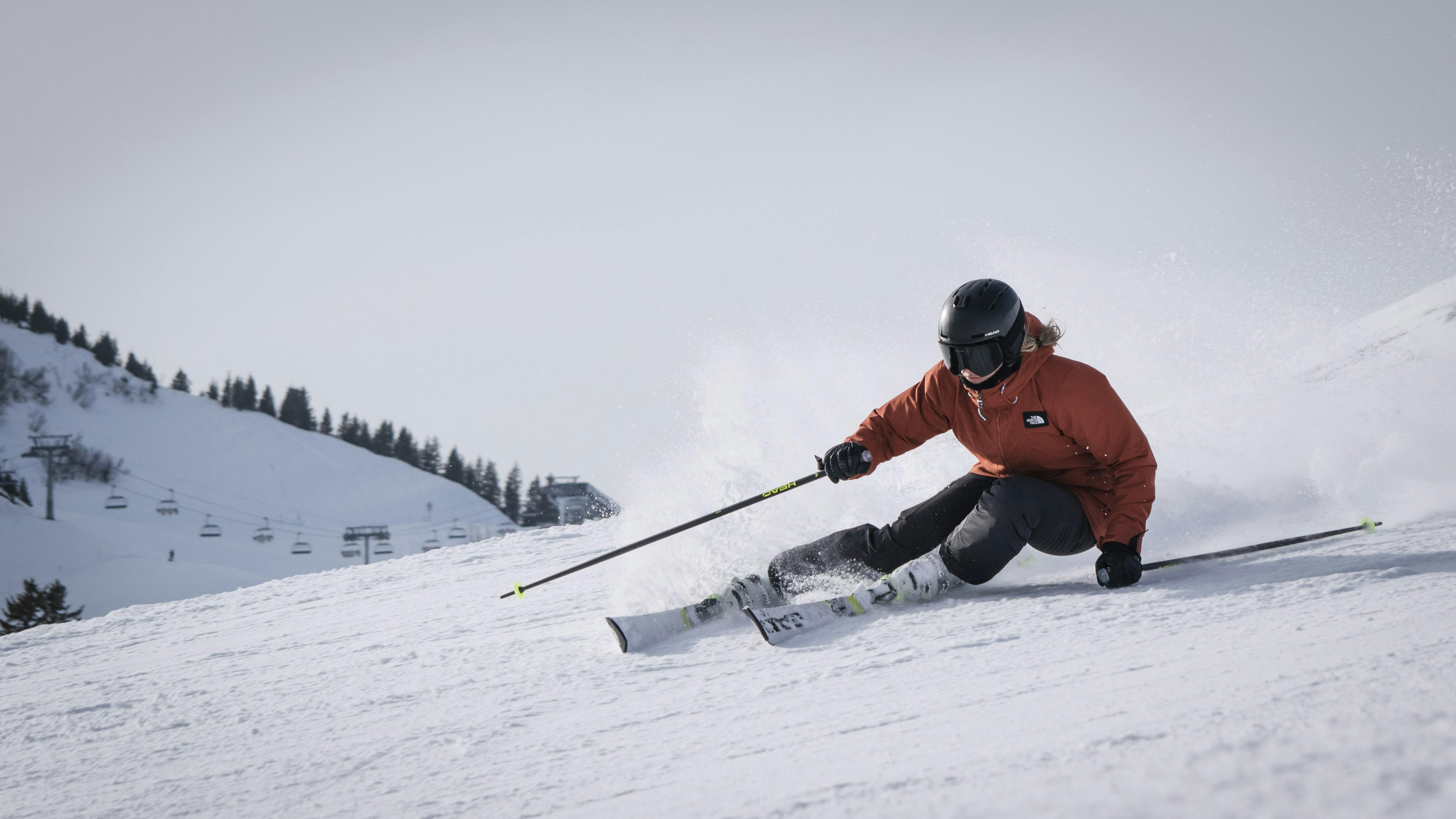 A skier in a red jacket bombing down a slope