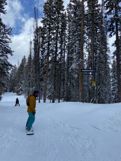 A snowboarder in snowboard gear turns down a run at a ski resort.