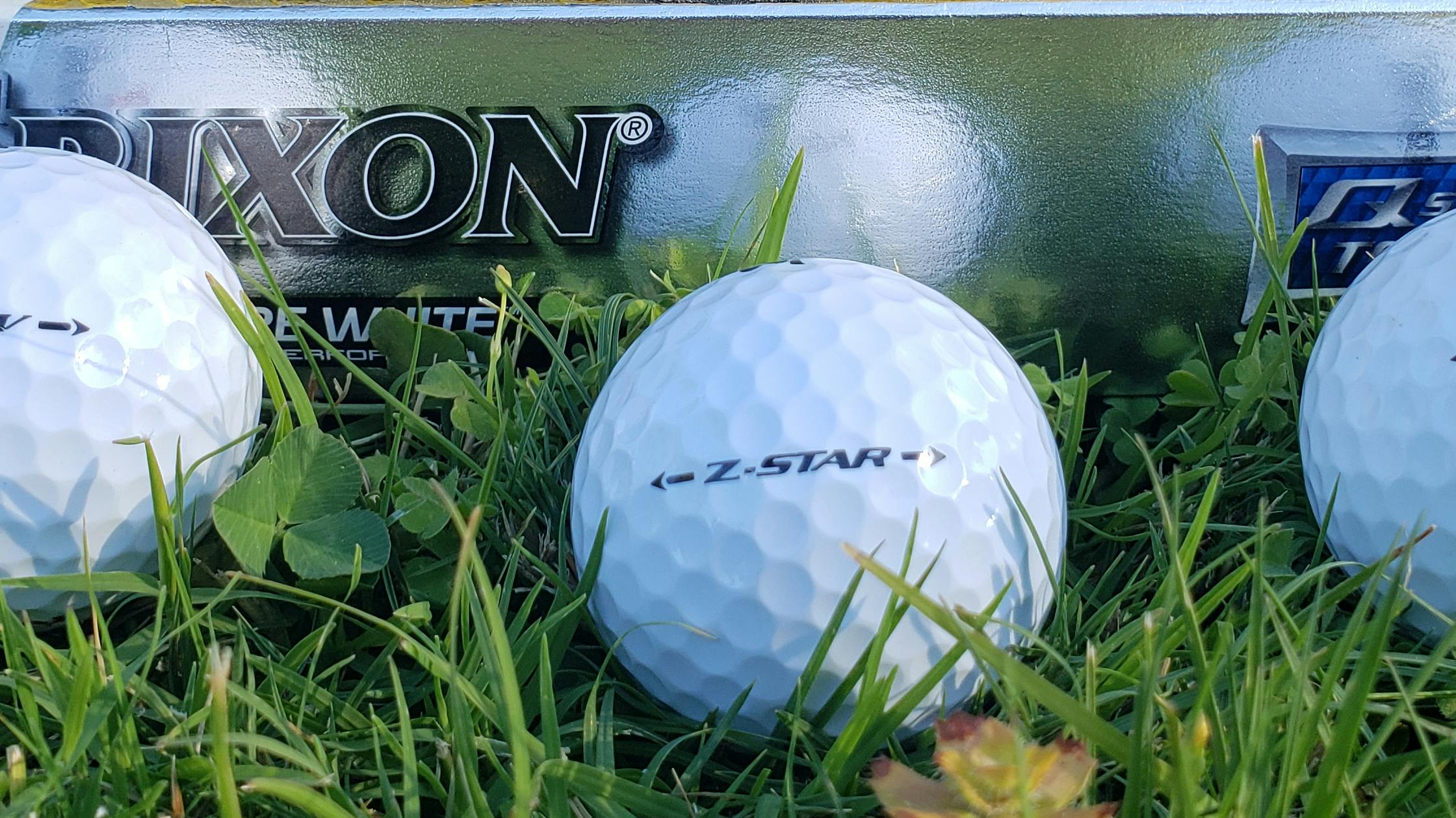 Three white golf balls with a silver box labeled "Srixon" behind them