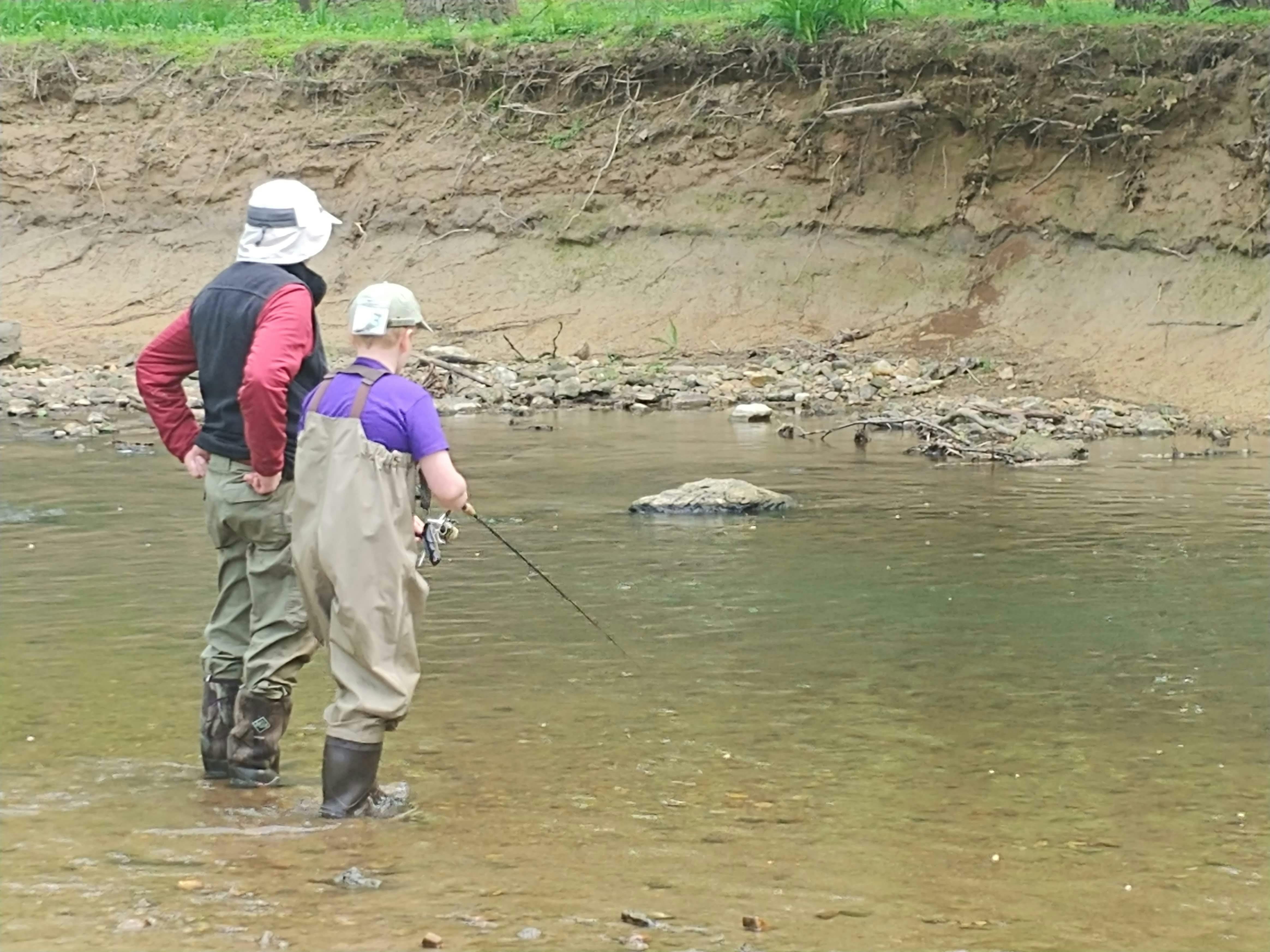 A father and son stand in the water in their waders. 