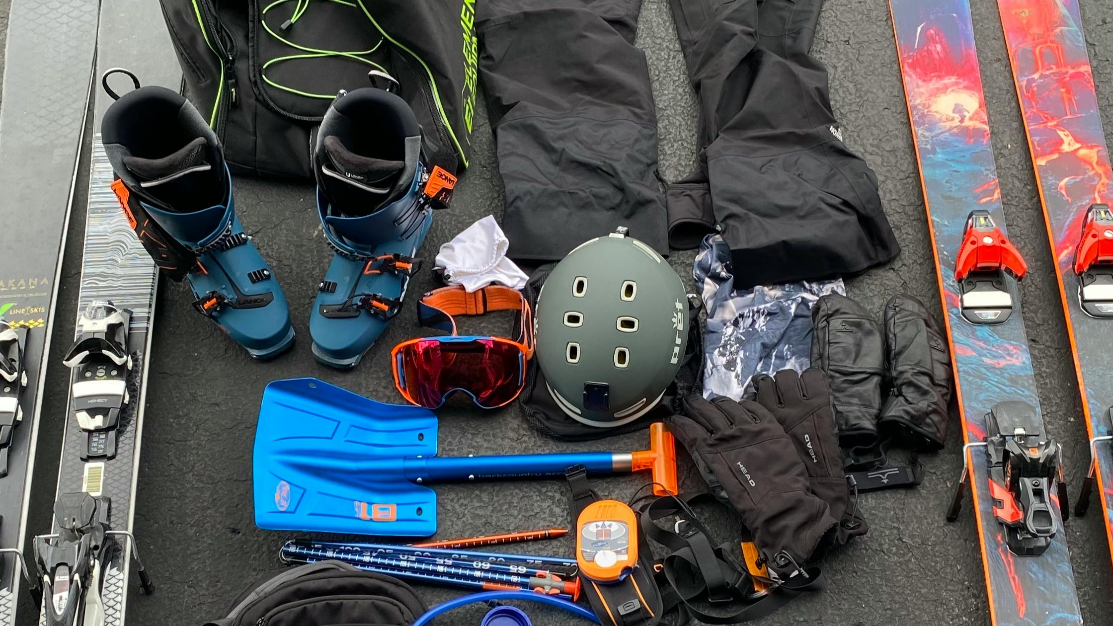 An image of the author's snow pants, helmet, shovel, goggles, gloves, buff, boot bag, 2 pairs of skis, and ski bag laying on asphalt. 