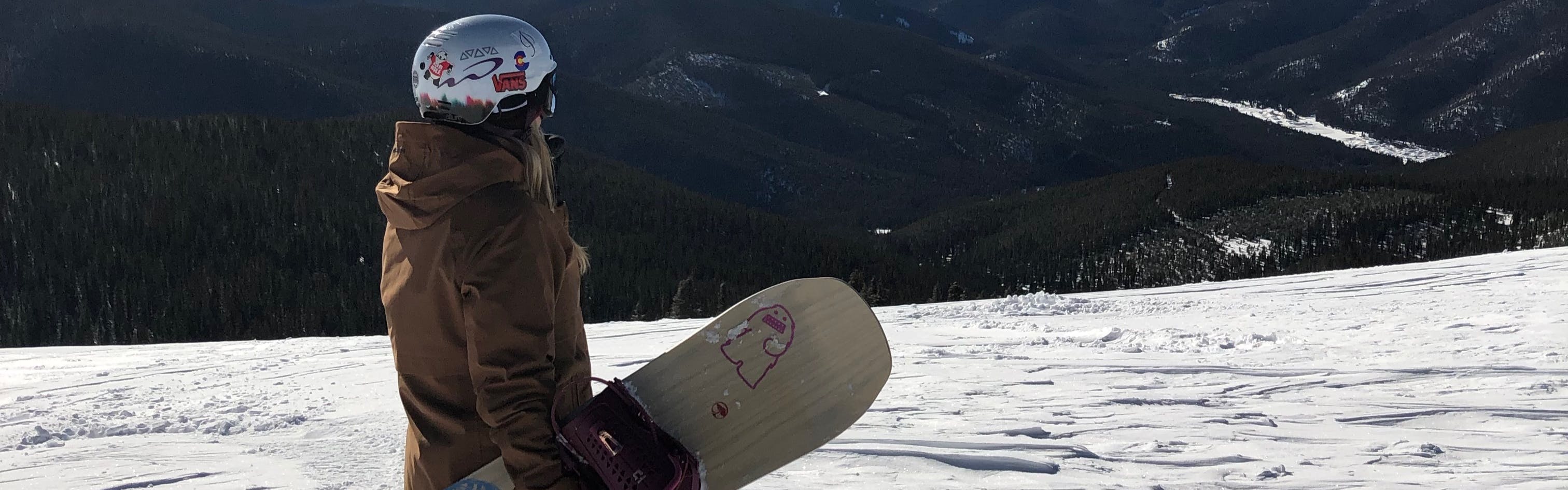 Curated expert Hannah S. standing on a snowy slope with her Arbor Swoon Camber Snowboard