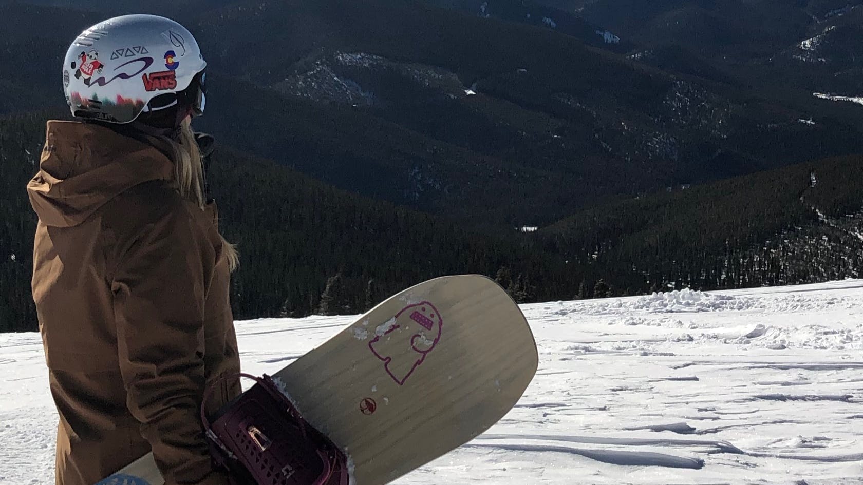 Curated expert Hannah S. standing on a snowy slope with her Arbor Swoon Camber Snowboard