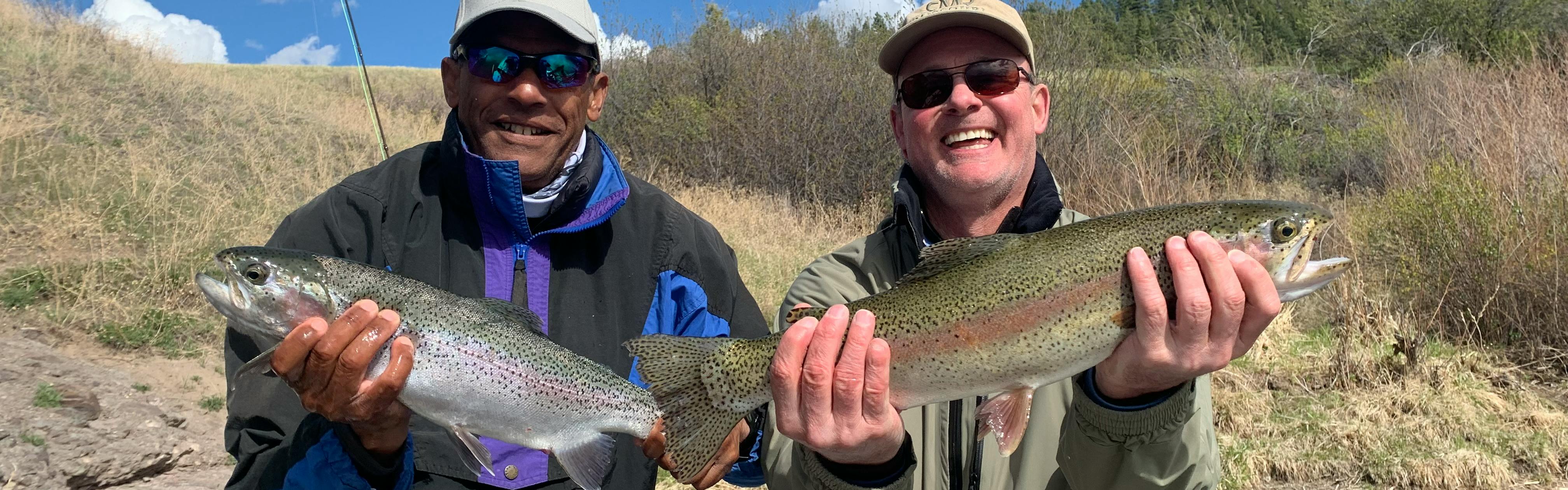 Two men smiling and each holding large trout. 
