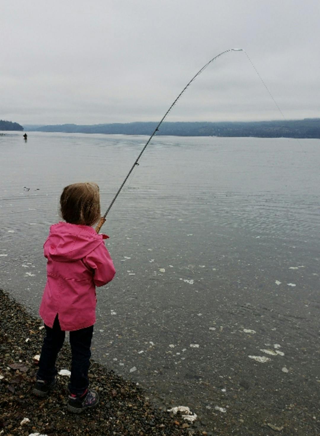 A little girl fishing on a bank. 