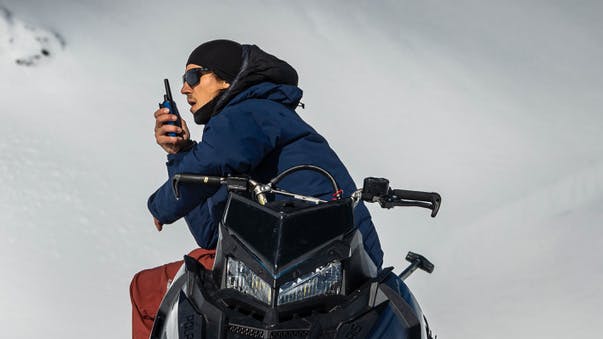 Edward Clem sits on a snowmobile and speaks into a walkie-talkie. 