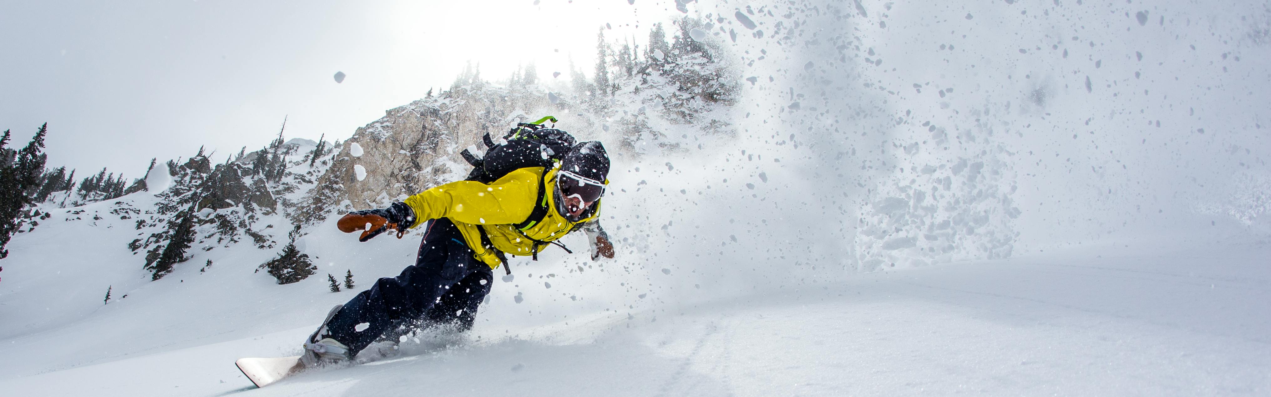 Snowboarder slicing through powder, sending a wave of fresh powder in his wake