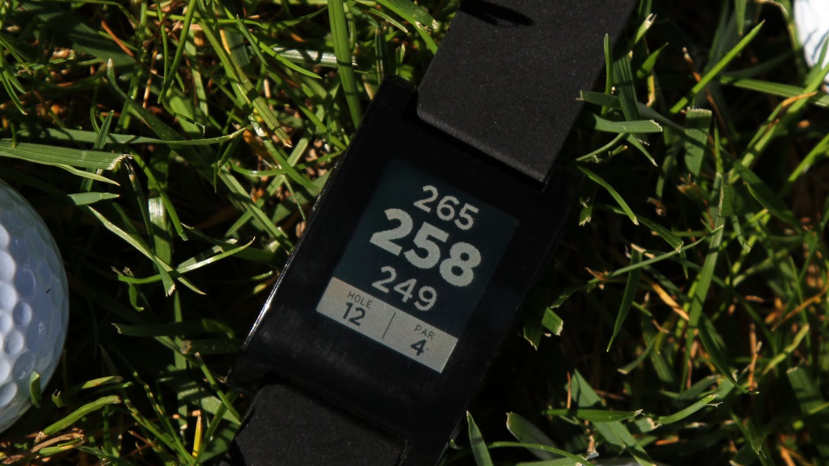 Pebble E-Paper Watch displaying Freecaddie golf rangefinder app. Also pictured, three golf-balls on grass