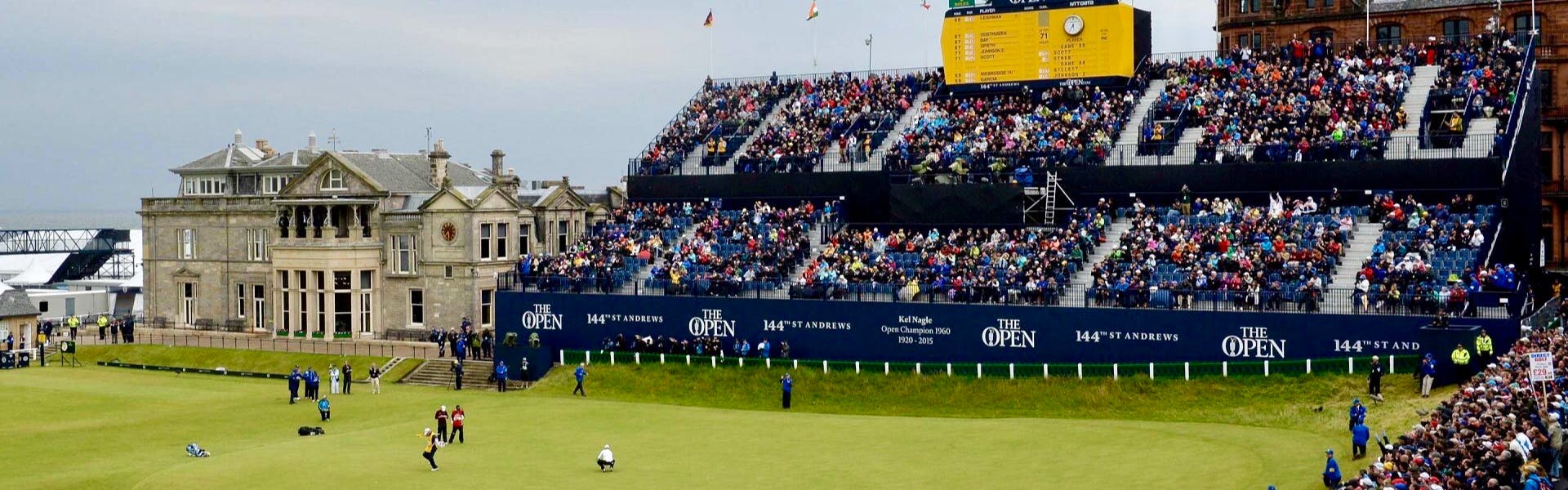 The 144th Open Championship at St. Andrews. The picture features a crowd in risers, players on a field, and a clubhouse. 