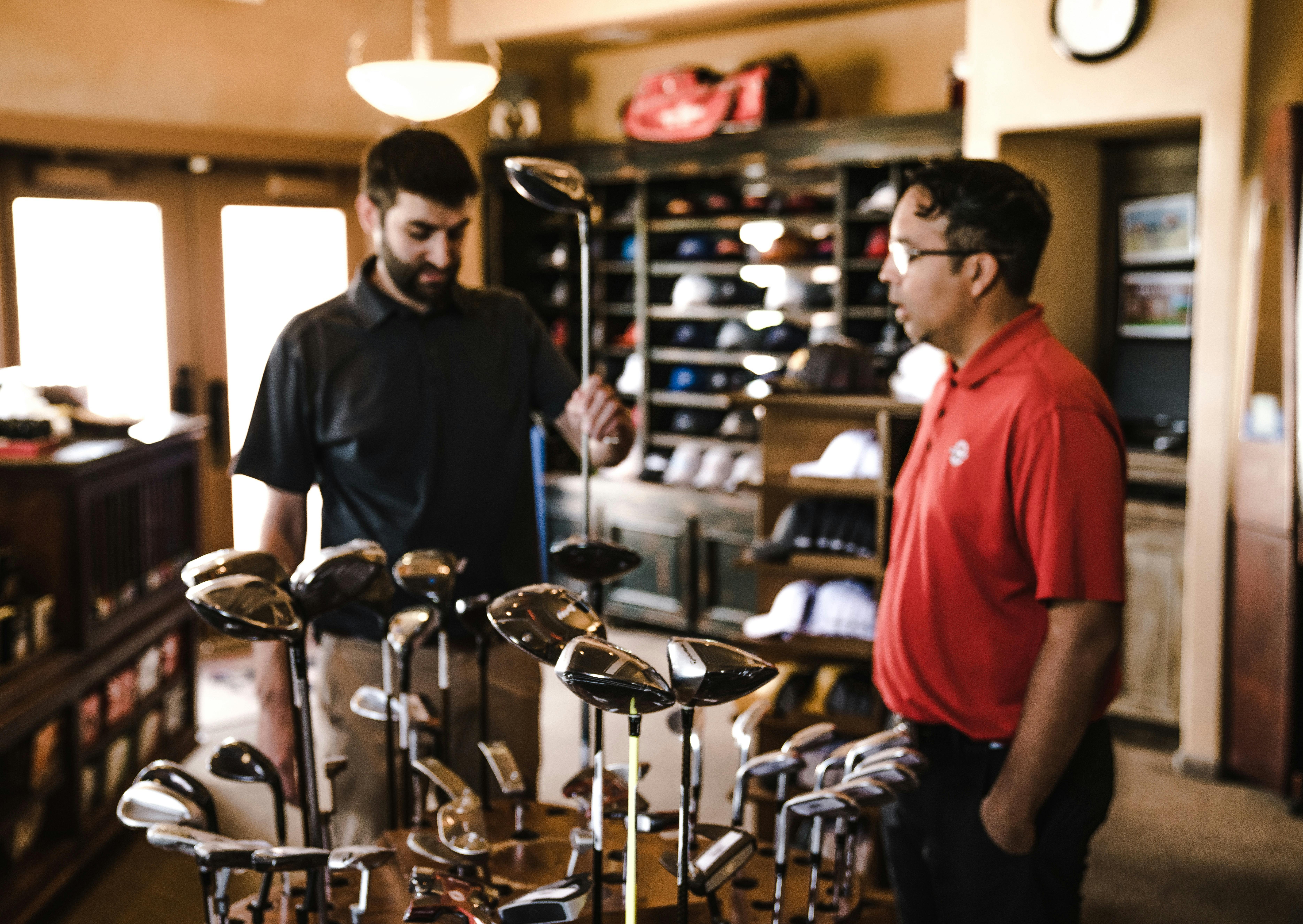 Two men examine golf clubs in a golf shop