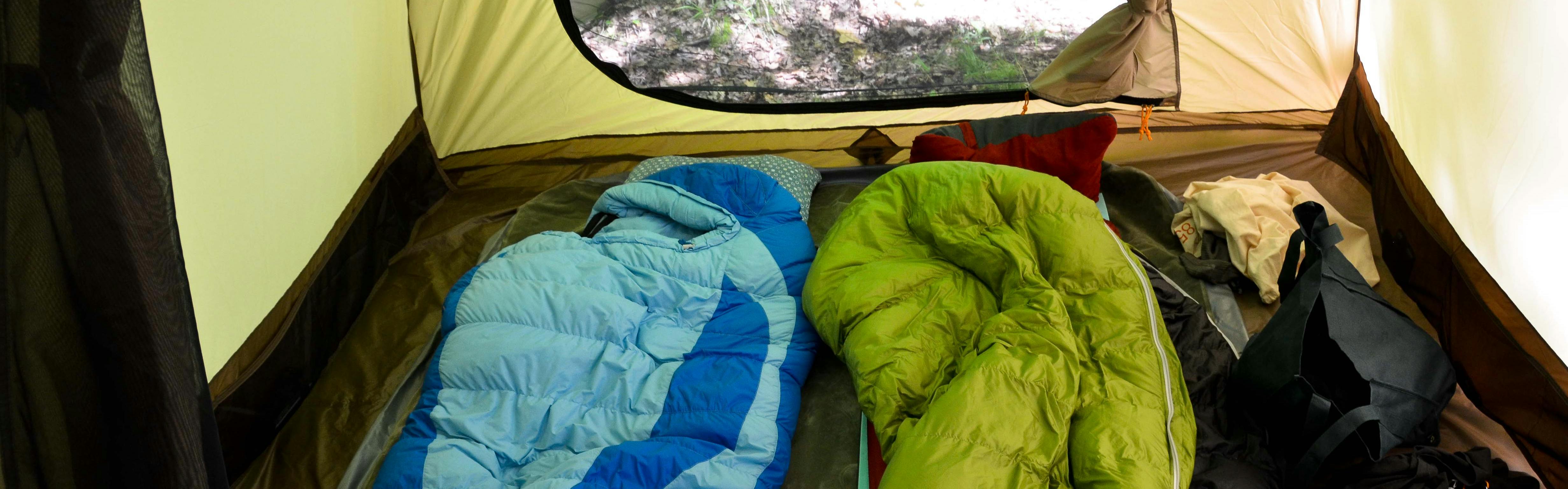 Two sleeping bags lay in a tent. One is green and one is blue.
