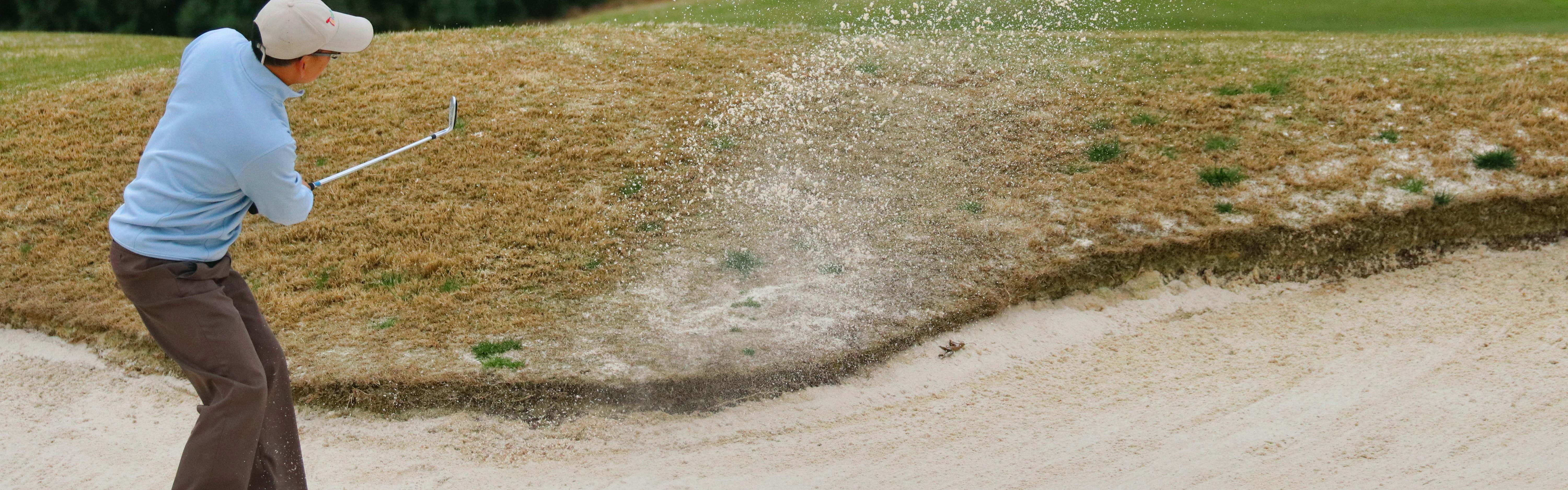A man swinging a golf club in a sand trap. 