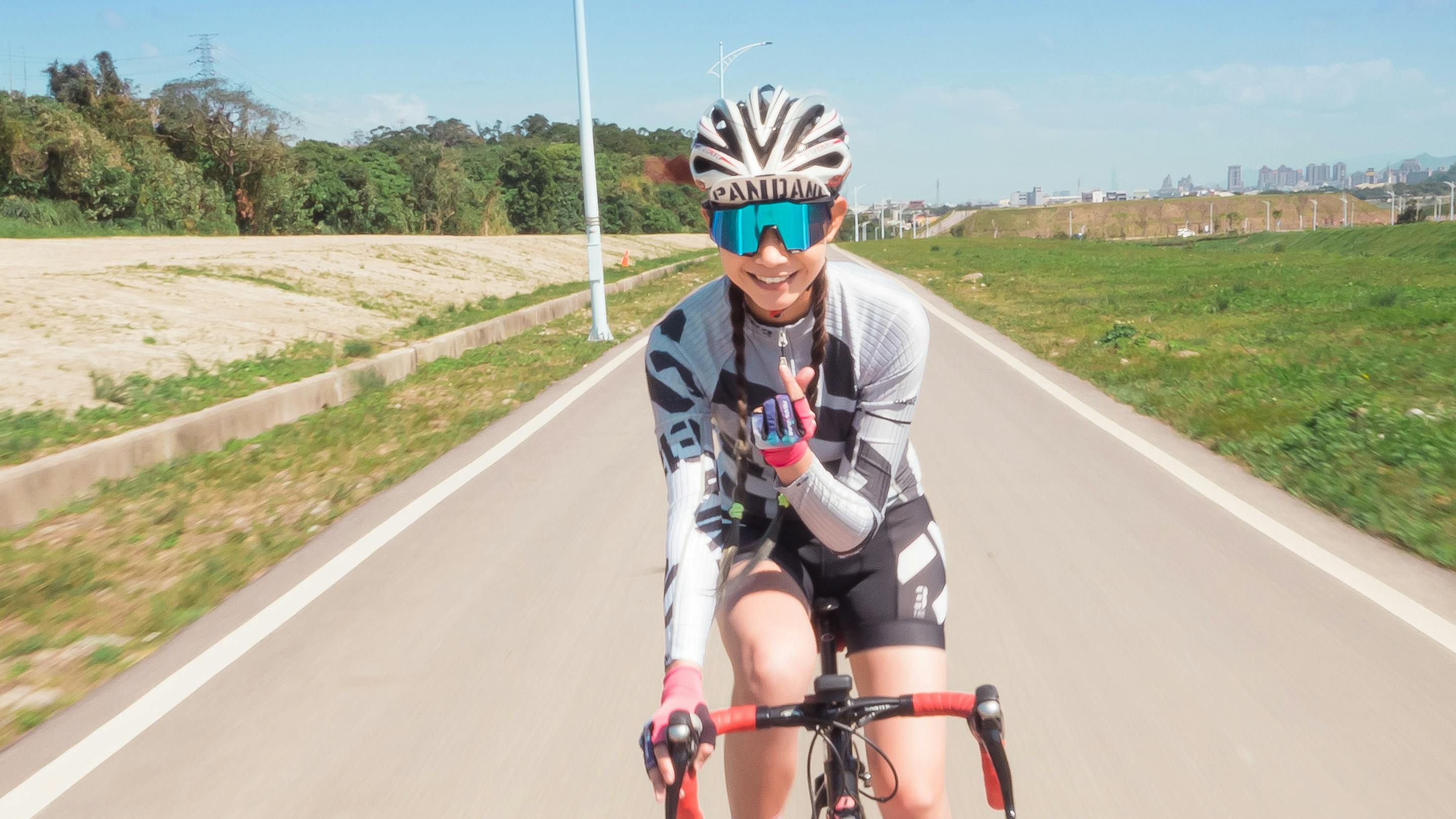 A woman road bikes and smiles at the camera in front of her.