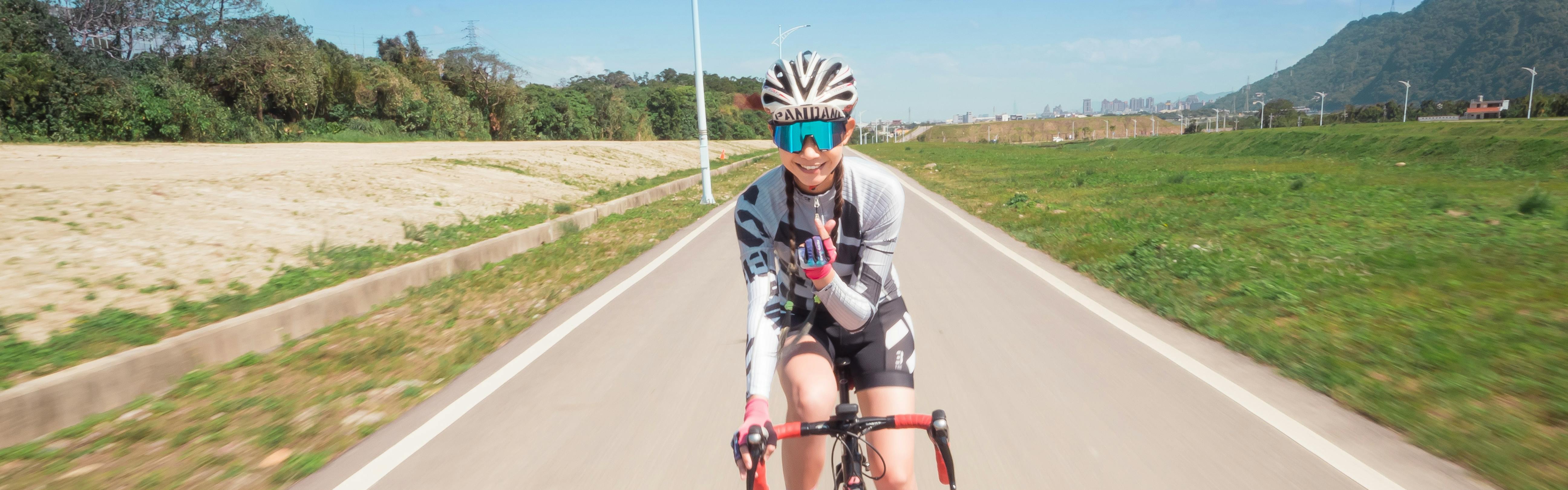 A woman road bikes and smiles at the camera in front of her.