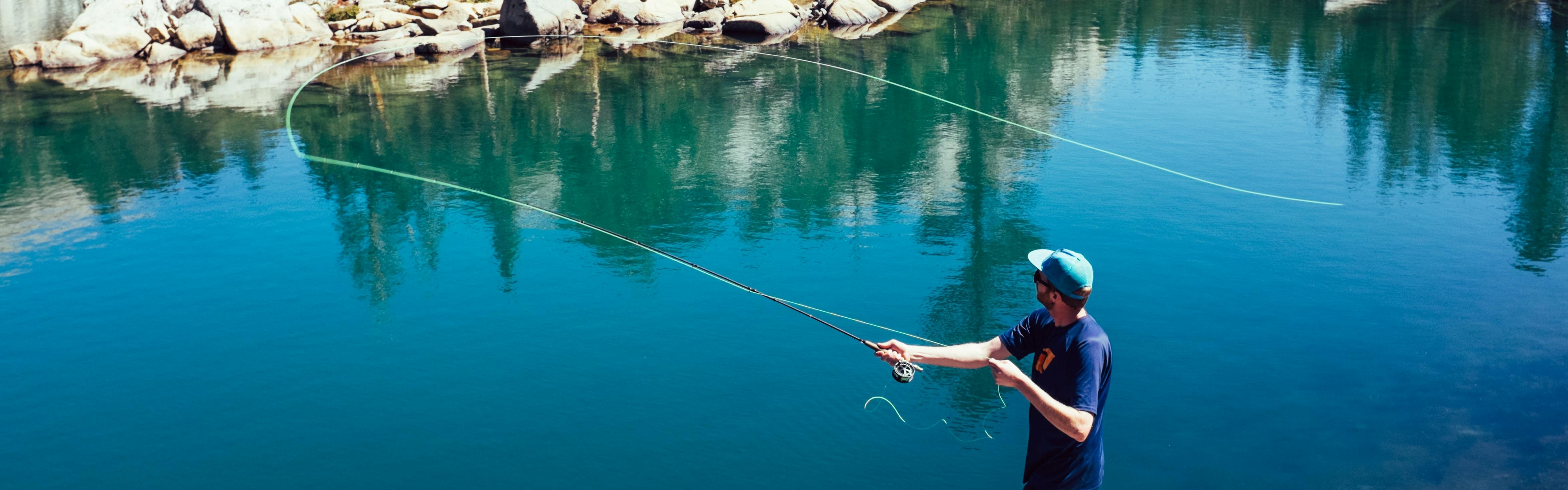A man casts a fly fishing rod over bright blue water.