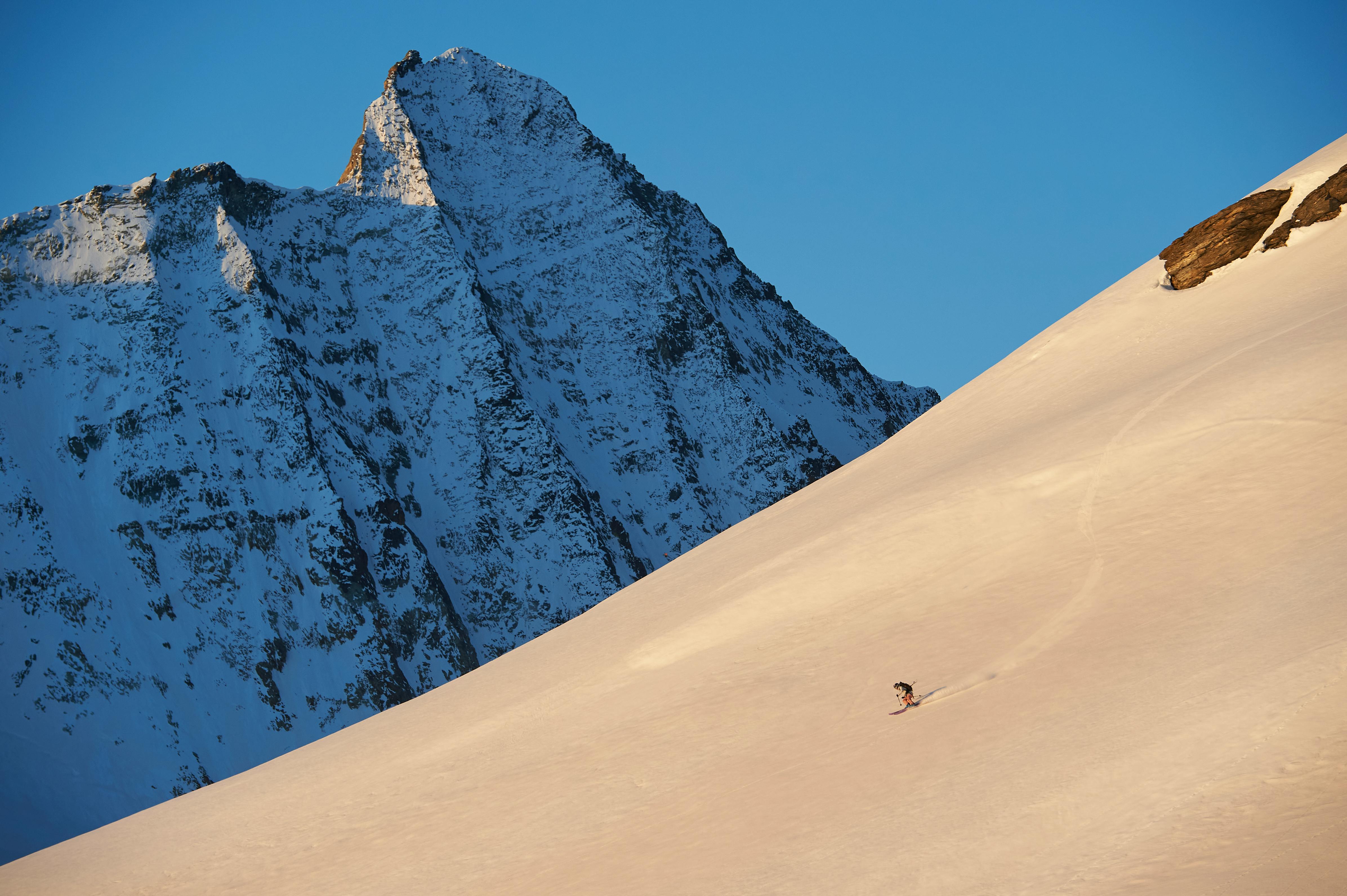 A solo skier skiing down a snowy backcountry mountain at sunrise