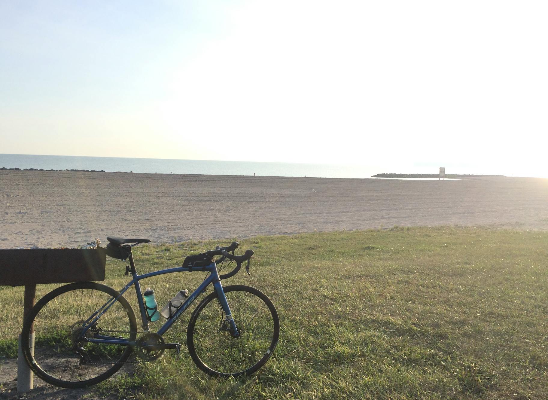 A bike is propped up in front of a sandy beach with an ocean in the background.