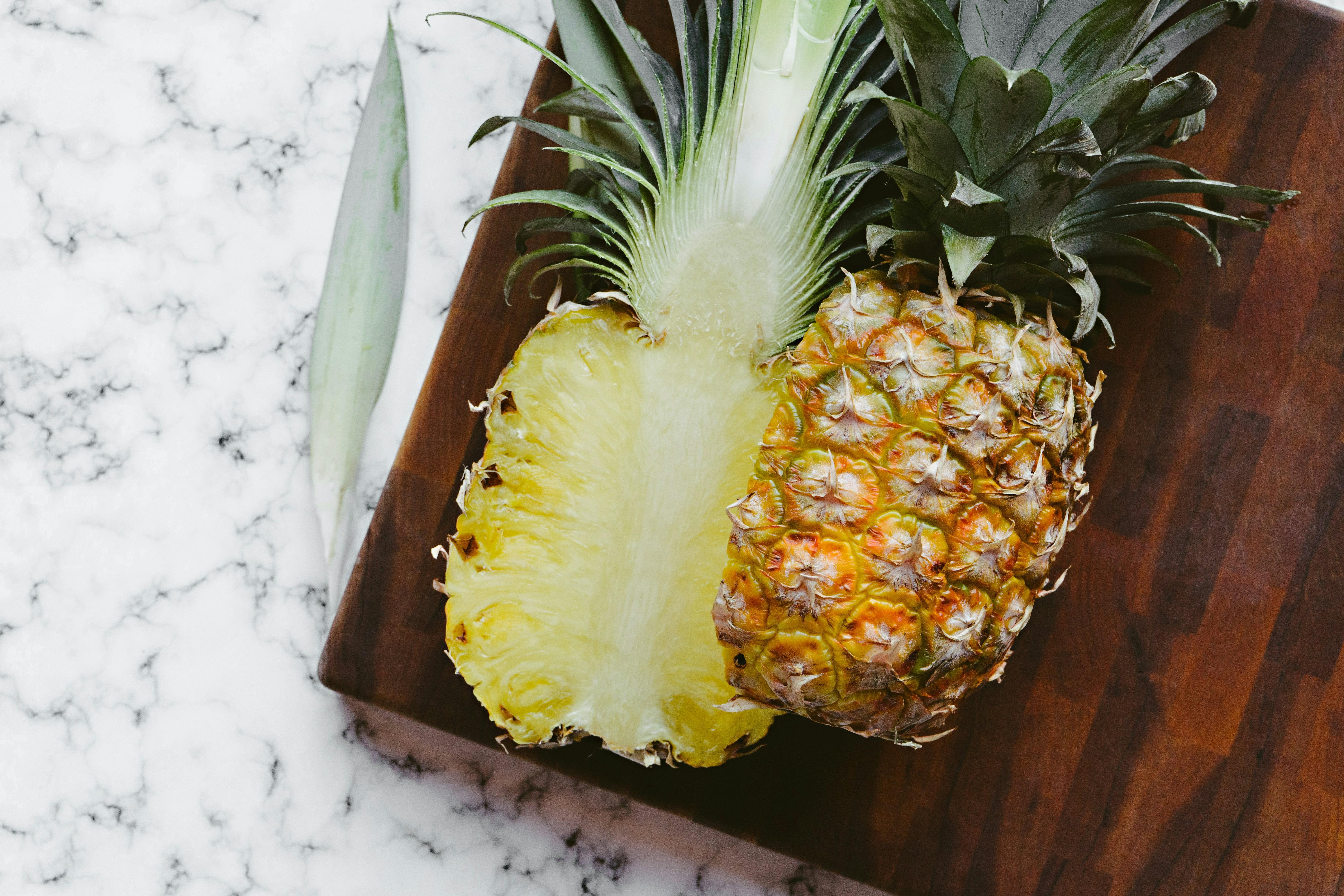A pineapple sliced in half on a wooden cutting board. 