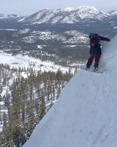 A snowboarder on the edge of a snowy mountain. 