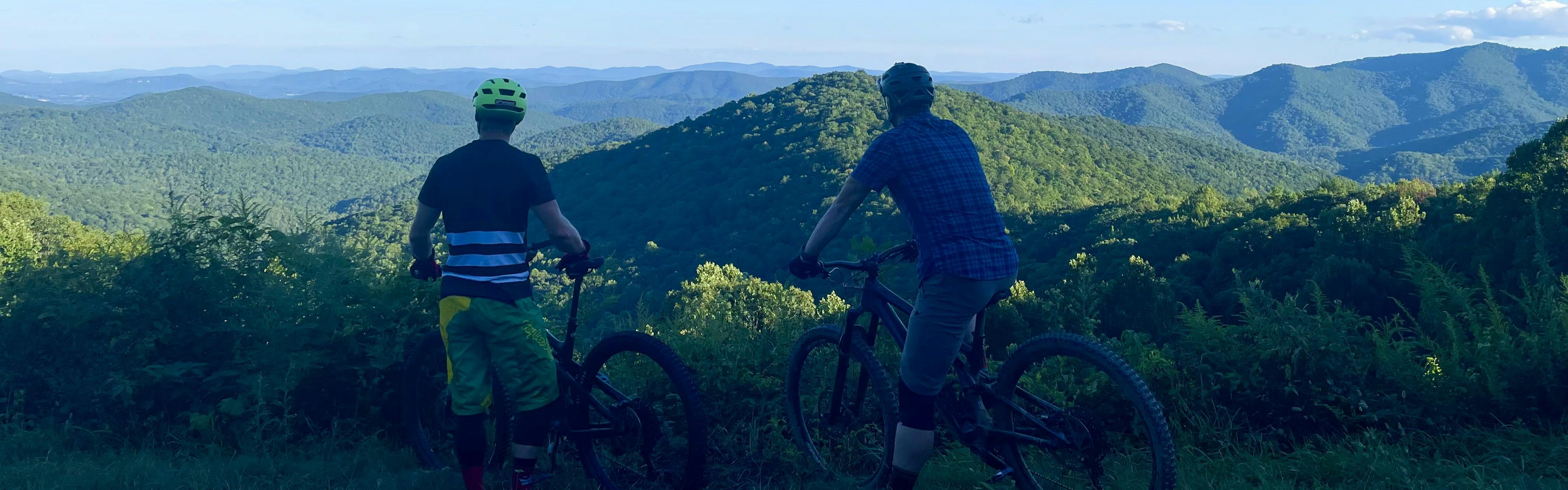 Two bikers standing with their bikes looking out over a mountain landscape. 