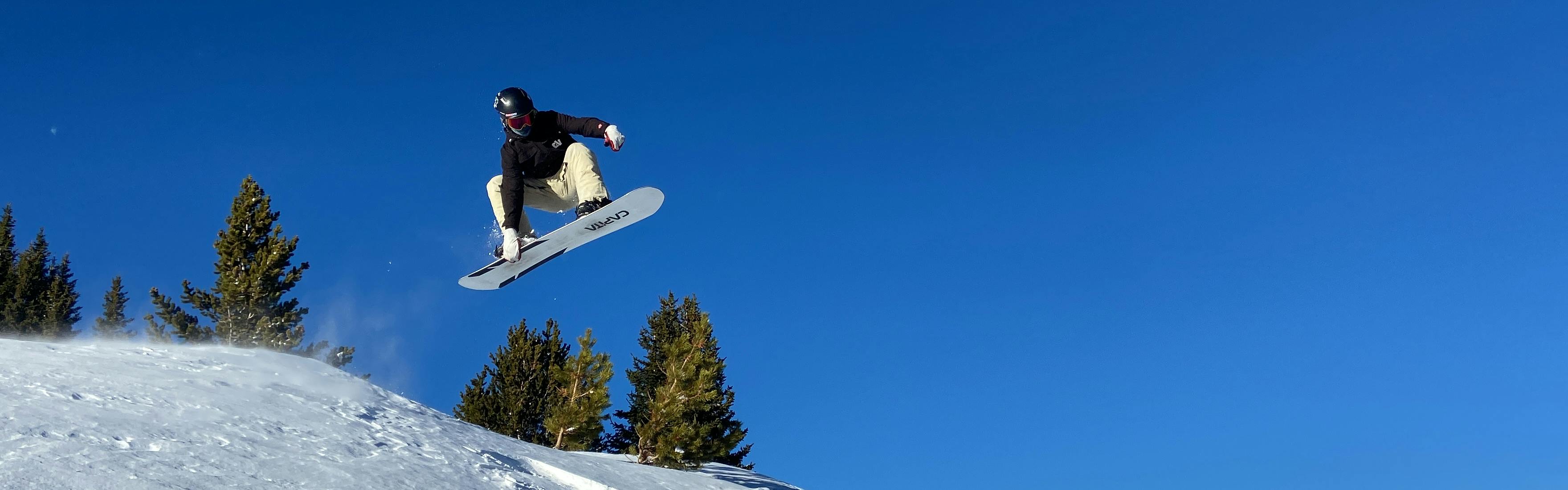 A man does a grab on a snowboard as he goes off a jump.