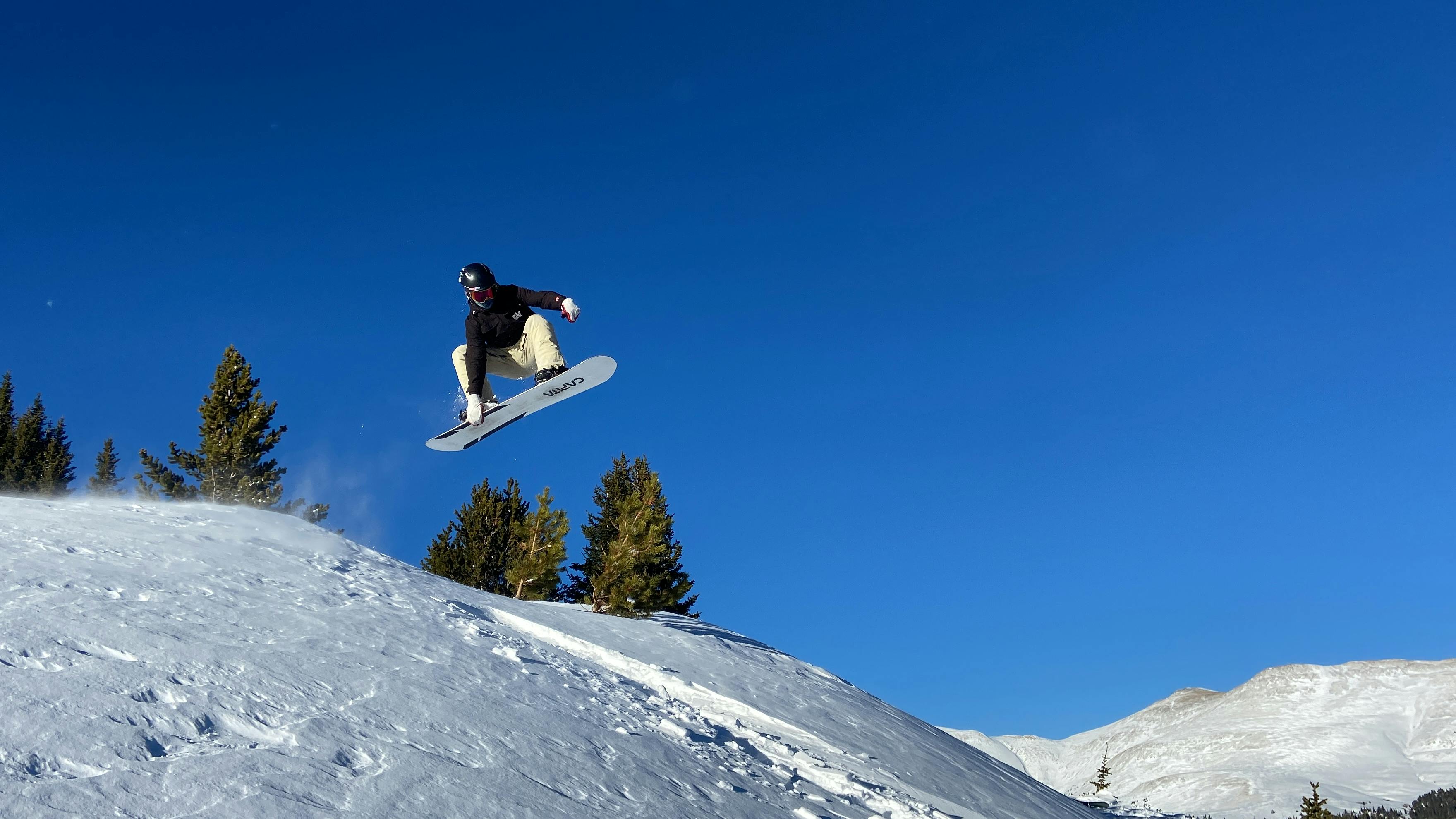 A man does a grab on a snowboard as he goes off a jump.