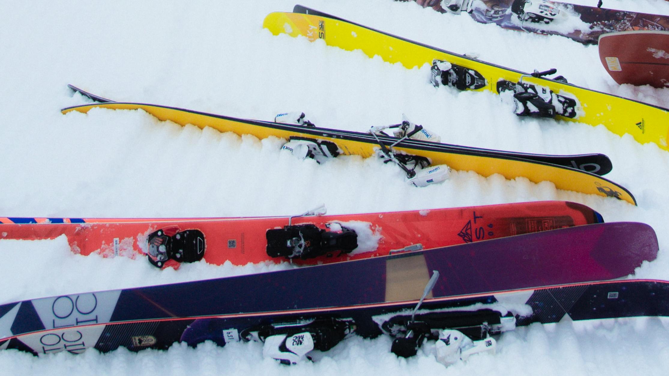 A row of brightly-colored skis lays down in the snow. 