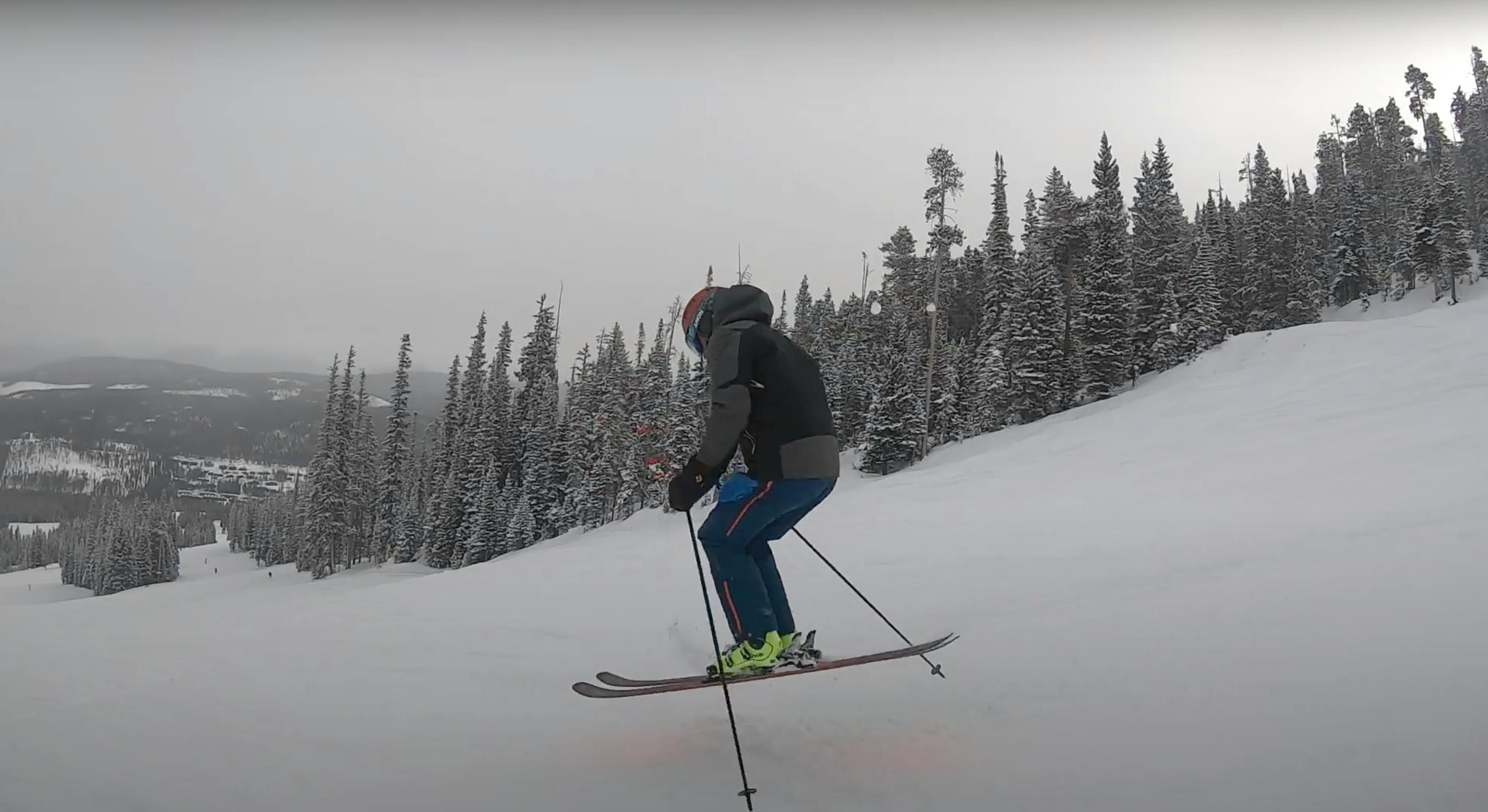 A man in blue pants and a grey jacket jumps in skis